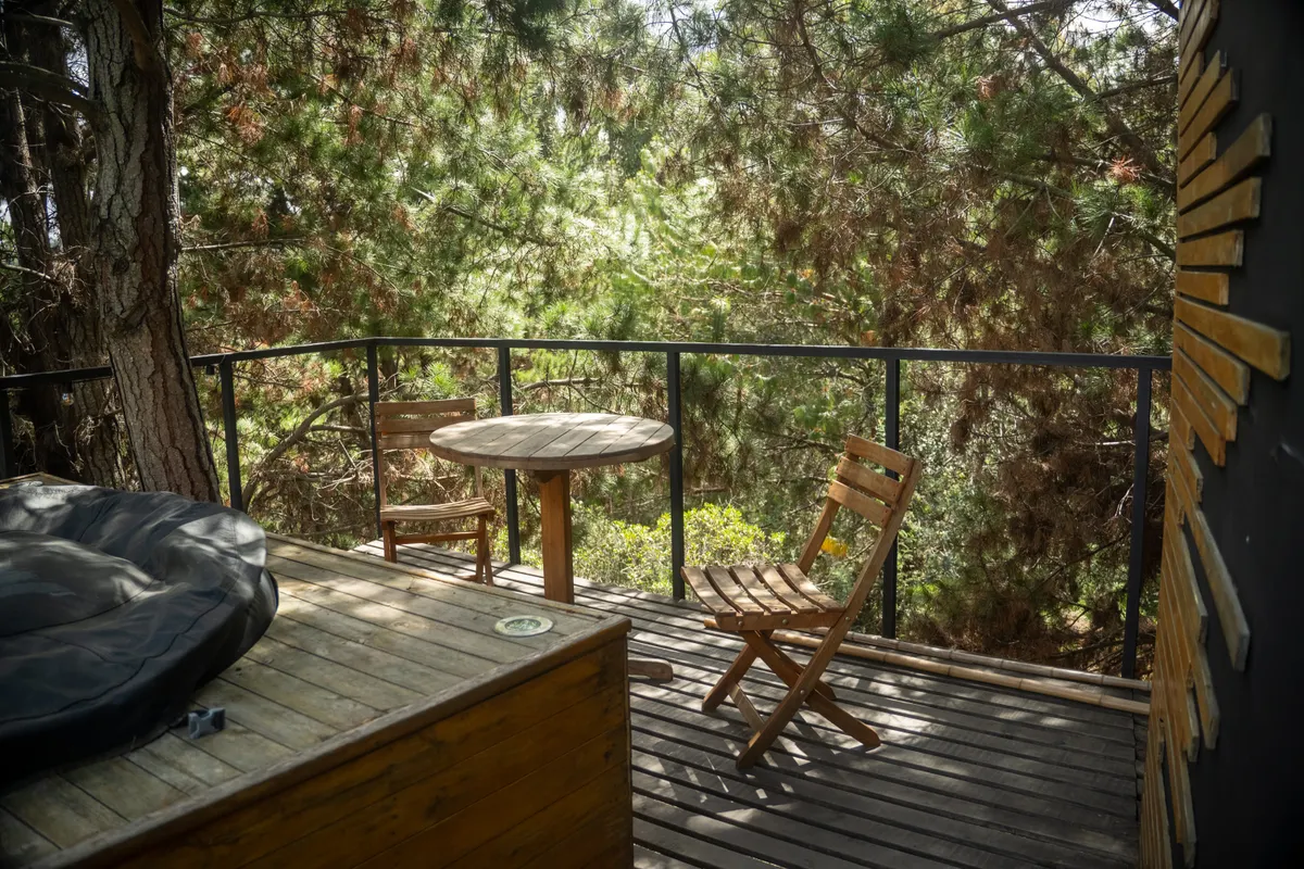 Outdoor balcony-style deck surrounded by trees with wooden chairs and table